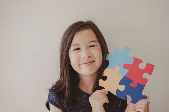 Smiling child holding colorful jigsaw puzzle pieces against a plain wall