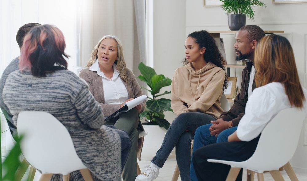 Small group in a bright counseling session, seated in a circle and talking with a facilitator.