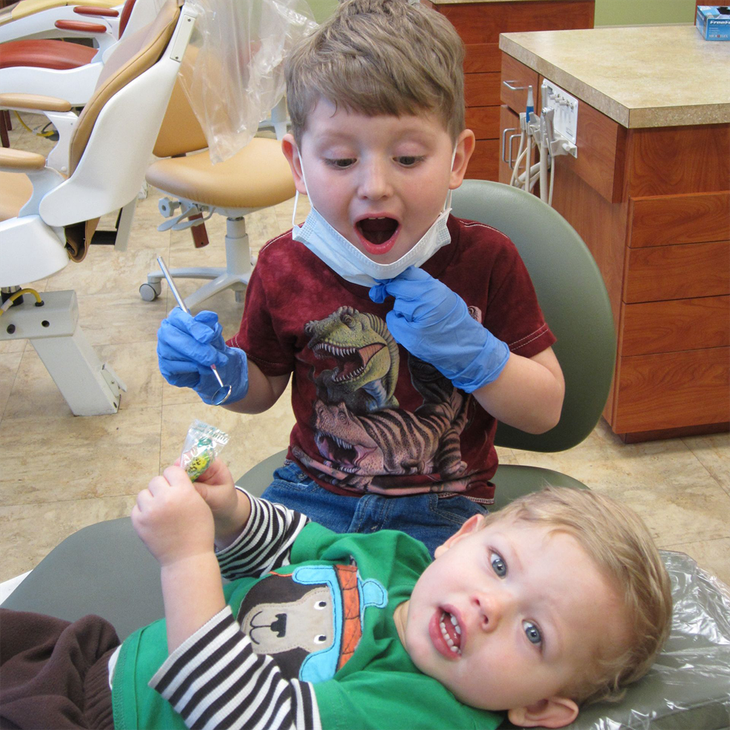 A young boy is brushing his teeth while holding a paper tooth.