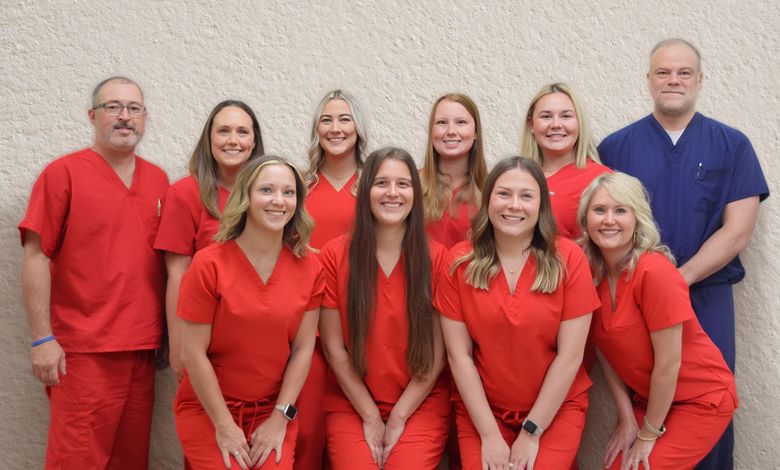 Group of ten people in red uniforms posing in two rows against a beige wall