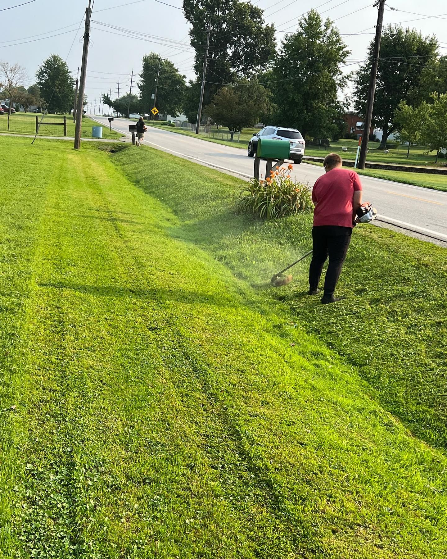 A woman is mowing the grass on the side of the road.