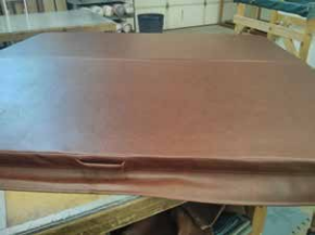 Brown hot tub cover resting on a support structure in a workshop.