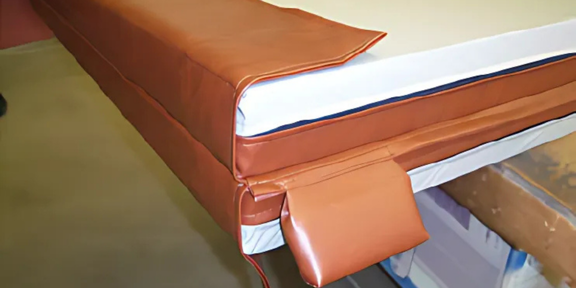 Brown leather-covered padded corner with white and blue accents. Shows a close-up of an upholstered edge.