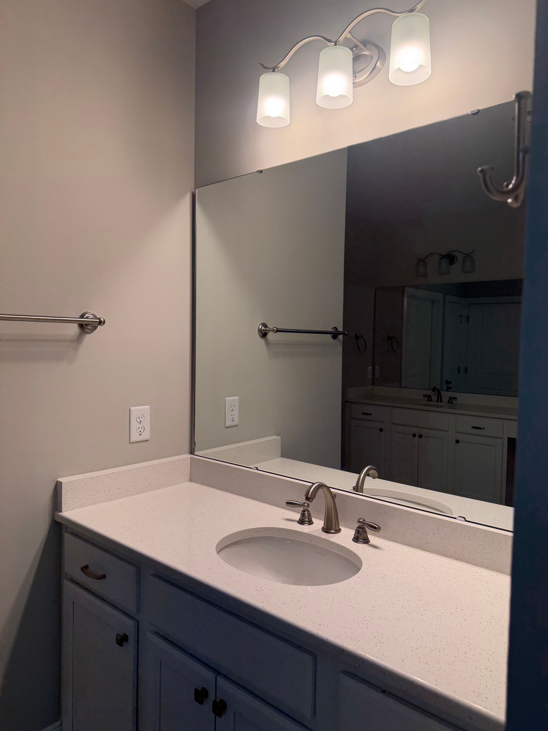 Bathroom vanity with mirror, white countertop, blue cabinets, and three light fixtures above.