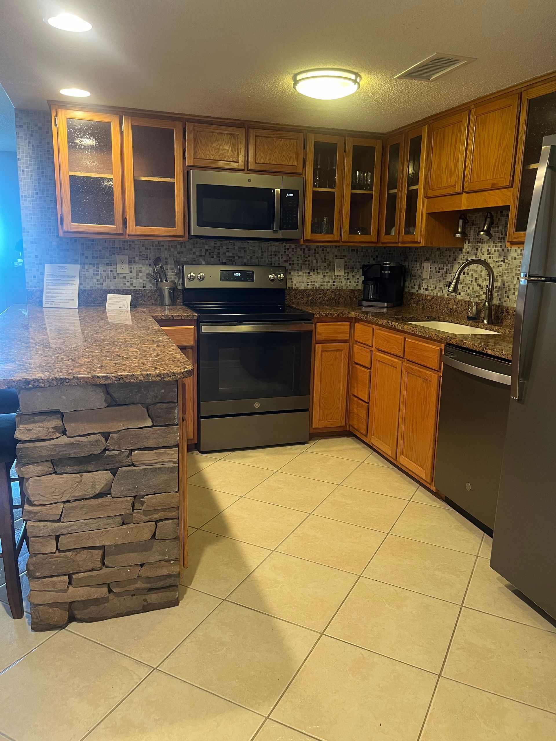 Kitchen with wooden cabinets, granite countertops, and stainless steel appliances. Includes a breakfast bar with a stone facade.