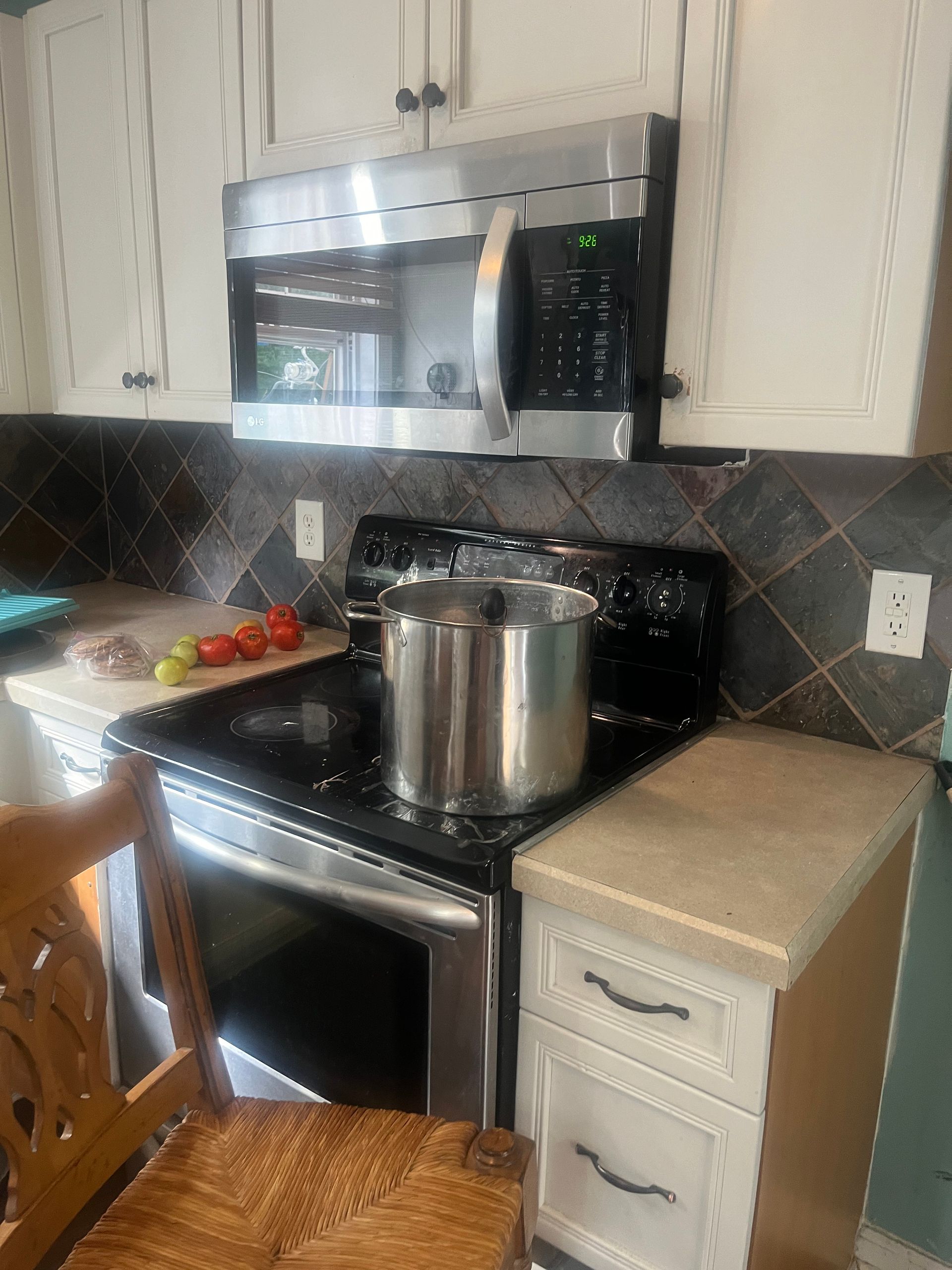 Kitchen with a stainless steel range, microwave, and a pot on the stovetop. Tomatoes and apples are on the counter.