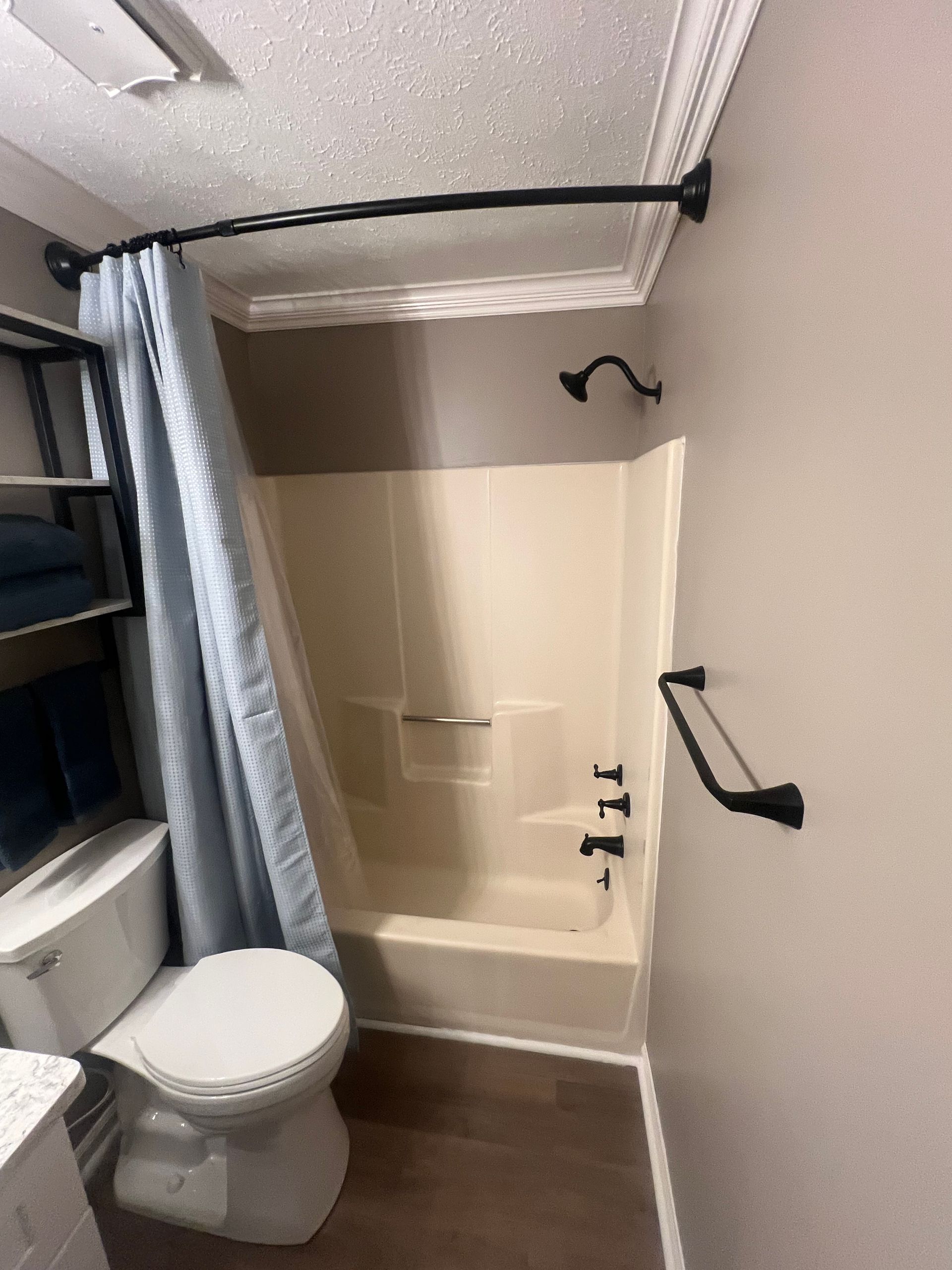 Bathroom with a beige bathtub, a blue shower curtain, a toilet, and black fixtures. The walls are painted gray and white.