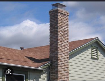 Roofer on a roof, inspecting a brick chimney in a neighborhood with homes and trees in the background.