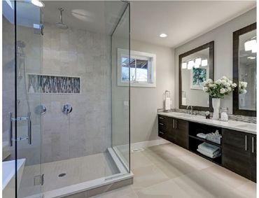 Modern bathroom with a dual-sink vanity, backlit mirrors, and a walk-in shower featuring blue tile and pebble flooring.