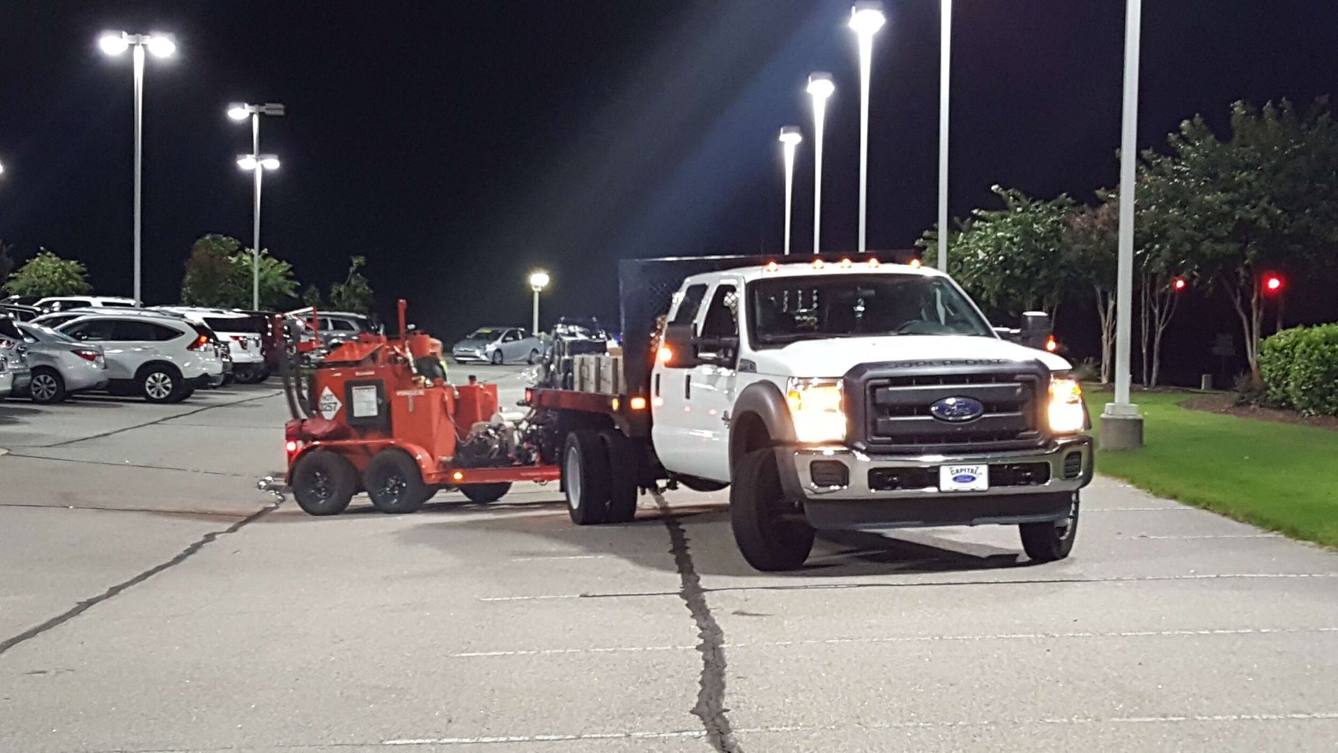 A white truck is towing a red trailer in a parking lot at night.