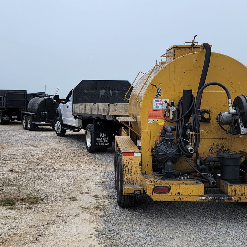 A yellow tanker truck is parked next to a white truck.