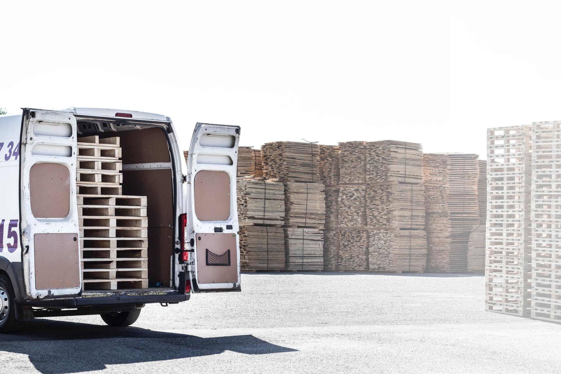 A white van is parked in front of a pile of wooden pallets.