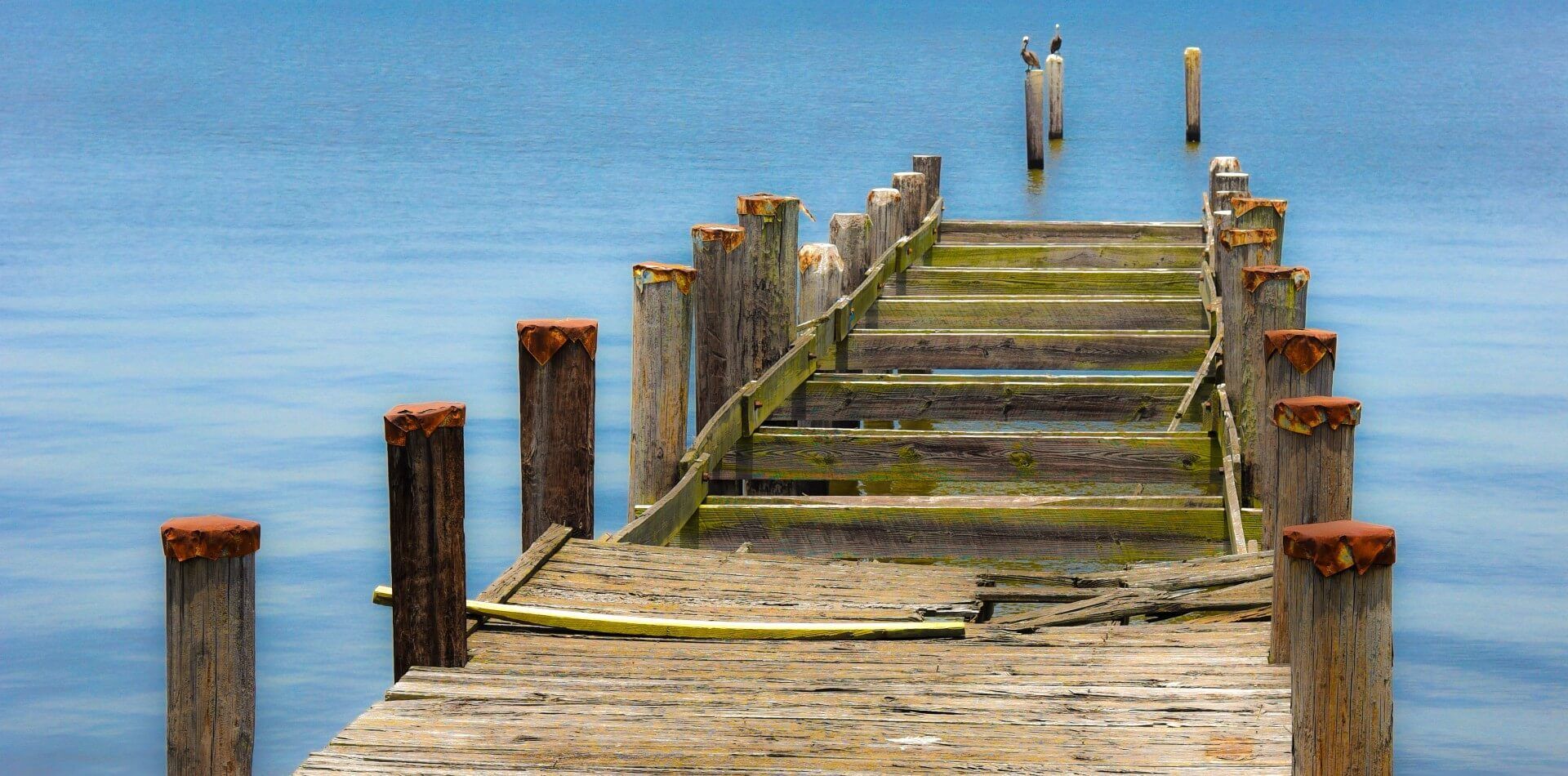 A wooden dock in need of repair leading into a body of water.