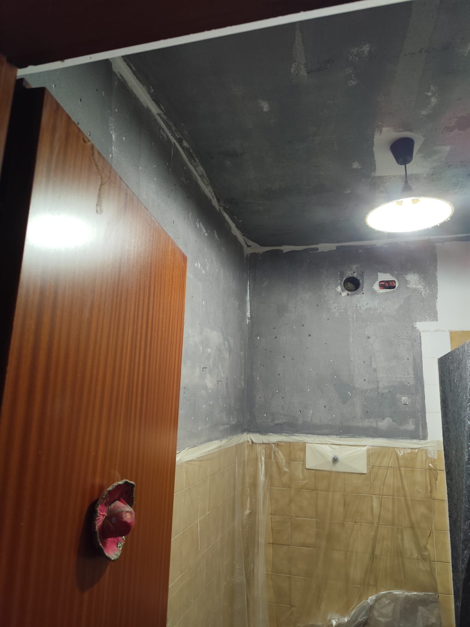 Bagno parzialmente ristrutturato con pareti grigie, porta in legno, piastrelle beige e lampadario a soffitto.