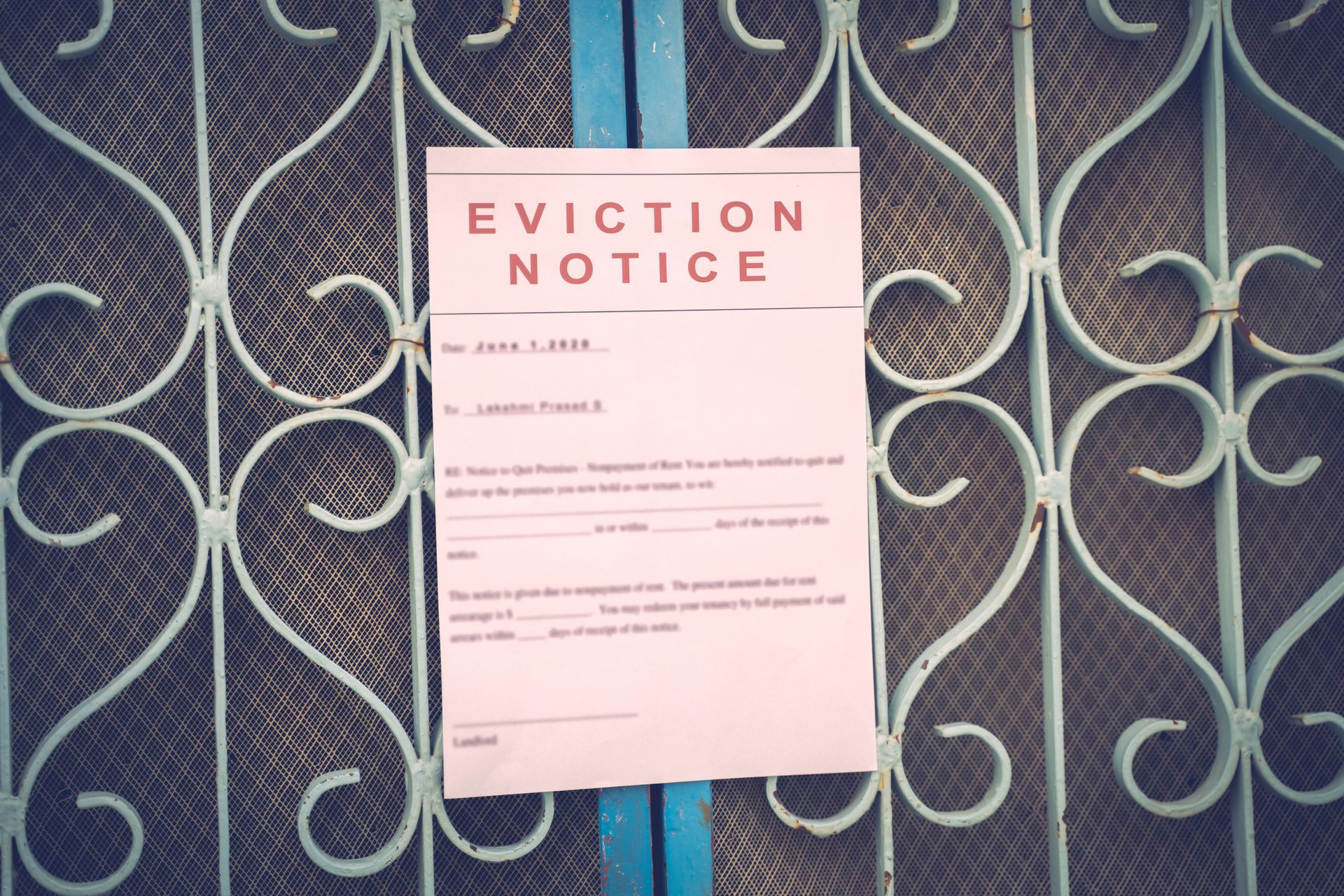 An eviction notice taped to a decorative, light blue metal gate.