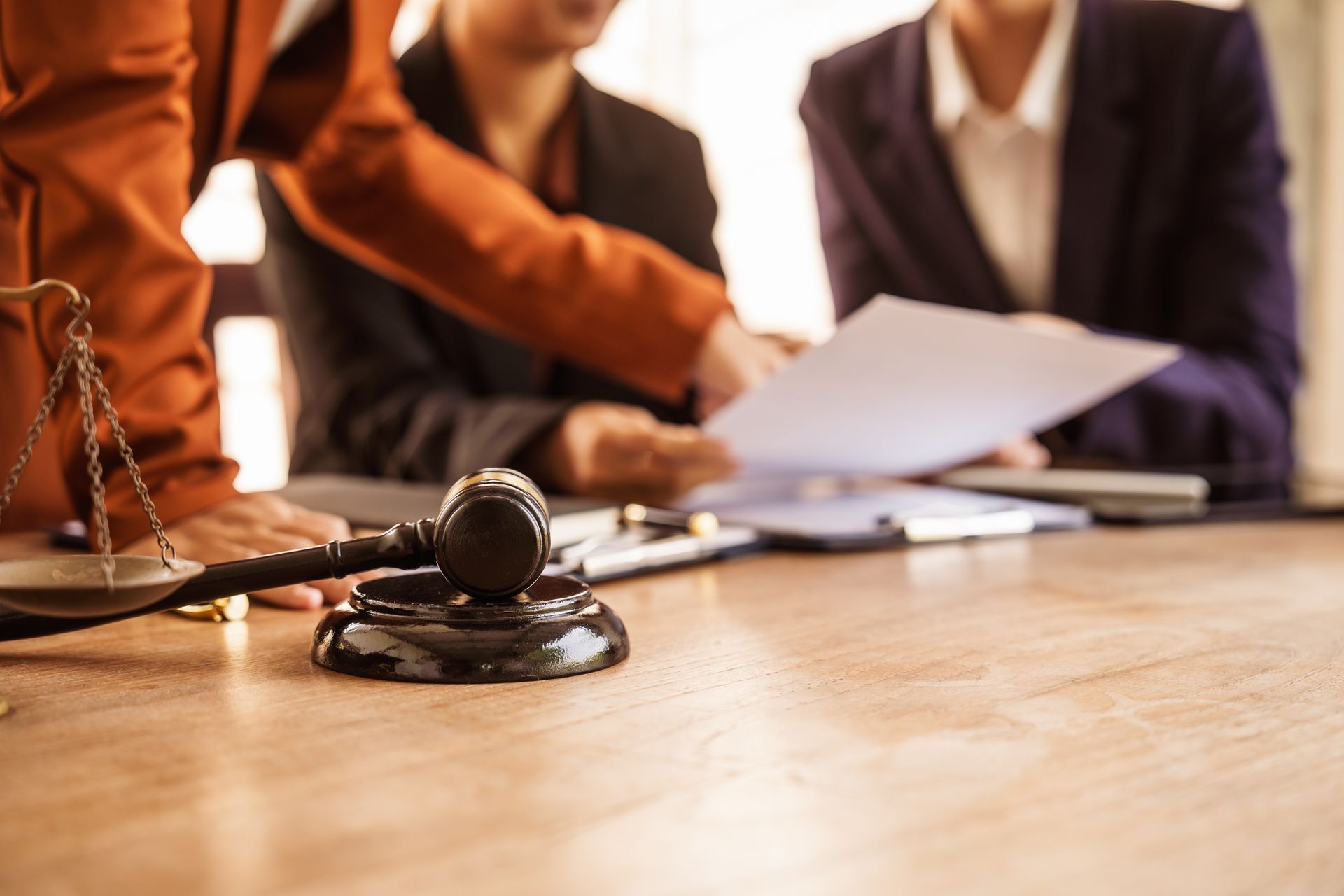 A gavel and scales of justice on a table with people reviewing legal documents in the background.