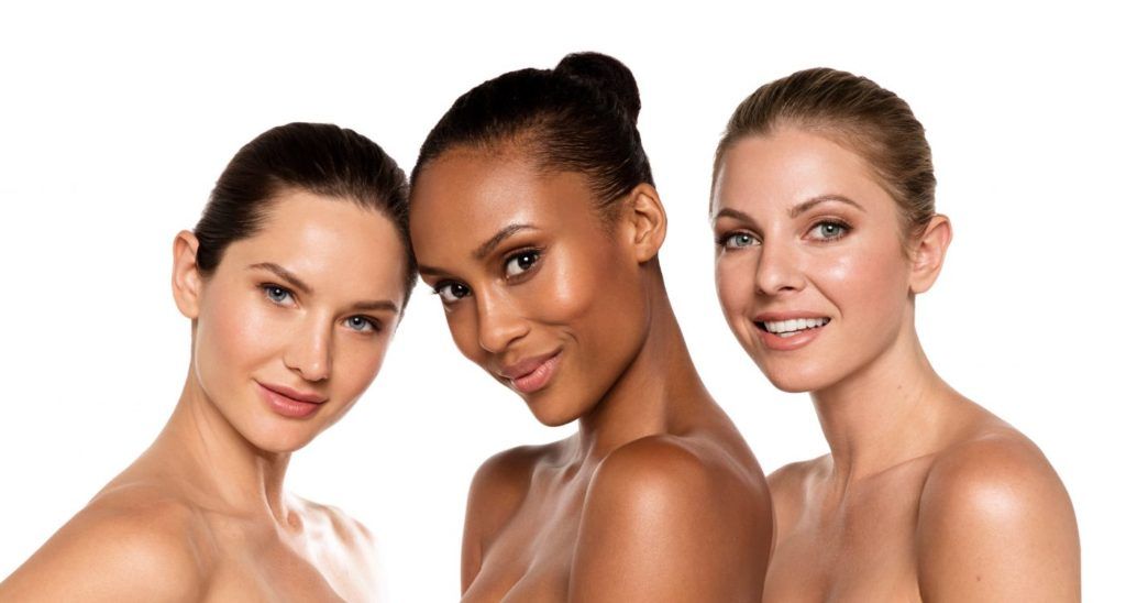 Three women with bare shoulders posing against a white background, smiling at the camera.