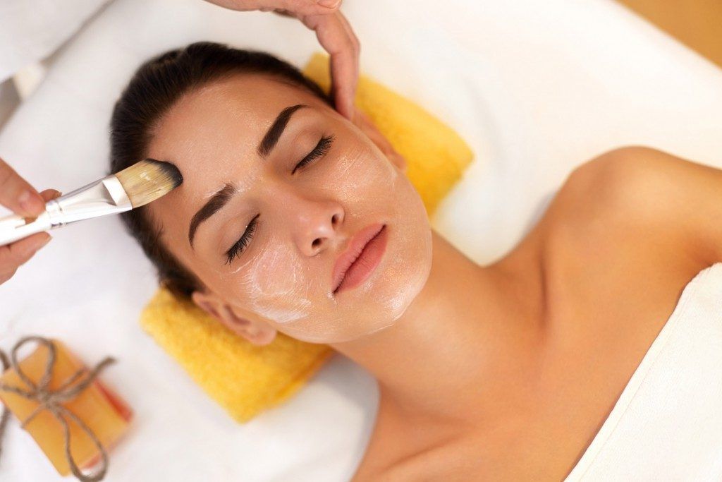 Woman receiving a facial treatment with a brush, lying on a towel in a spa setting