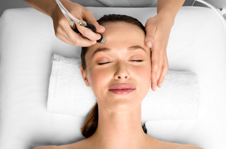 Woman receiving a facial treatment with a device while lying on a spa bed with eyes closed