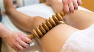 Spa therapist using a hot stone roller on a client's back during a massage