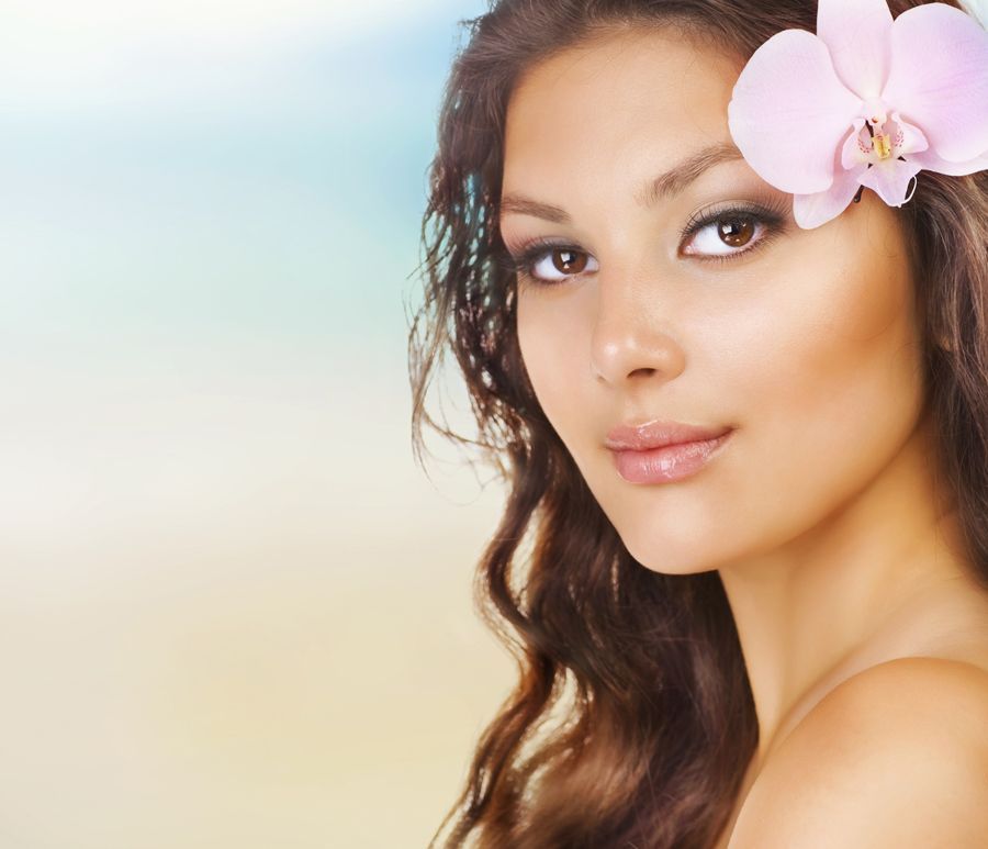 Portrait of a woman with a pink flower in her hair against a soft pastel background