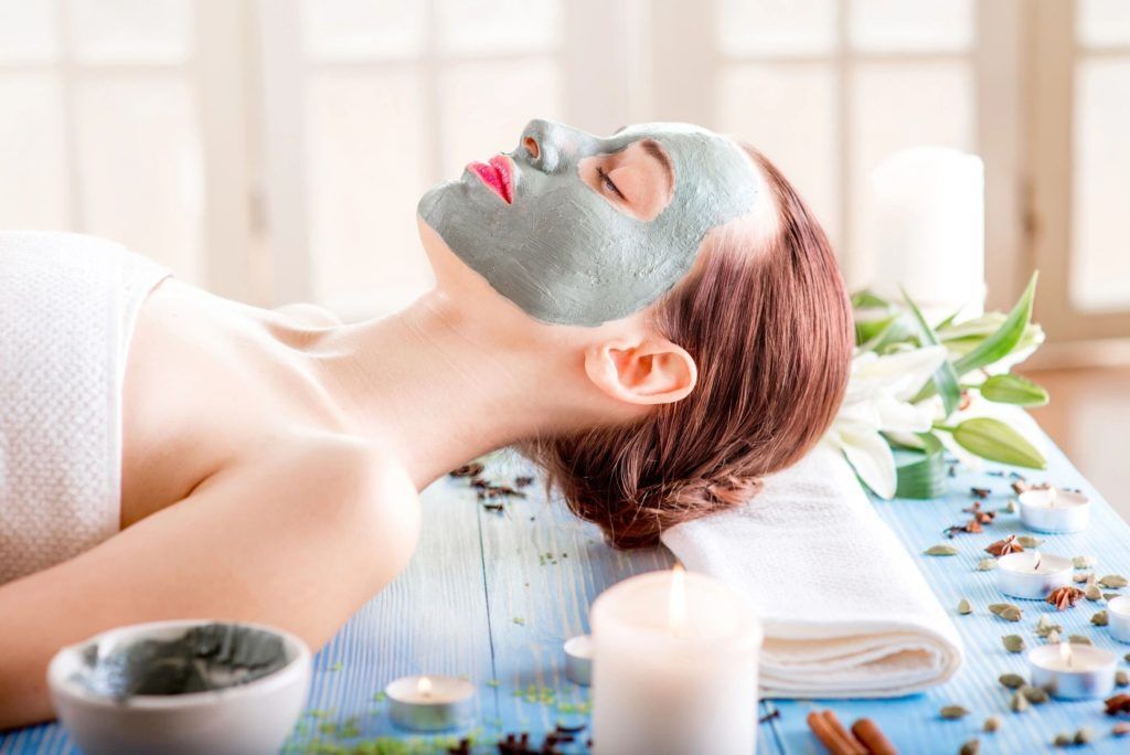 Woman relaxing with a green facial mask during a spa treatment, surrounded by candles and flowers