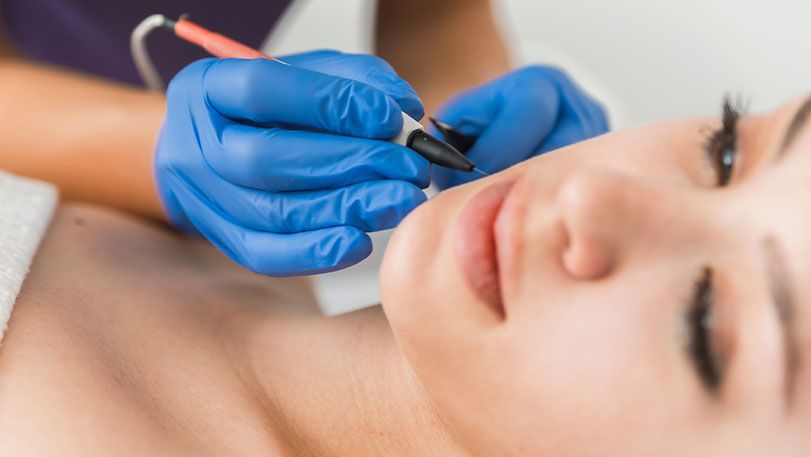 Gloved hands applying makeup near a woman’s closed eye in a beauty treatment