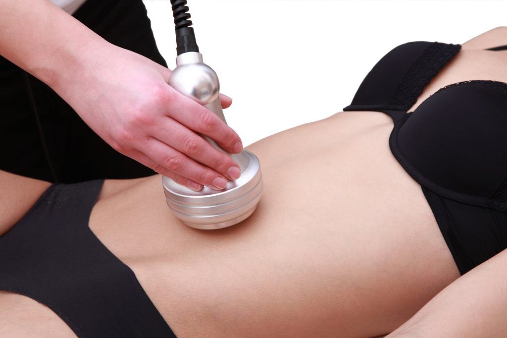 Hand using a massage device on a person’s bare abdomen during a spa treatment