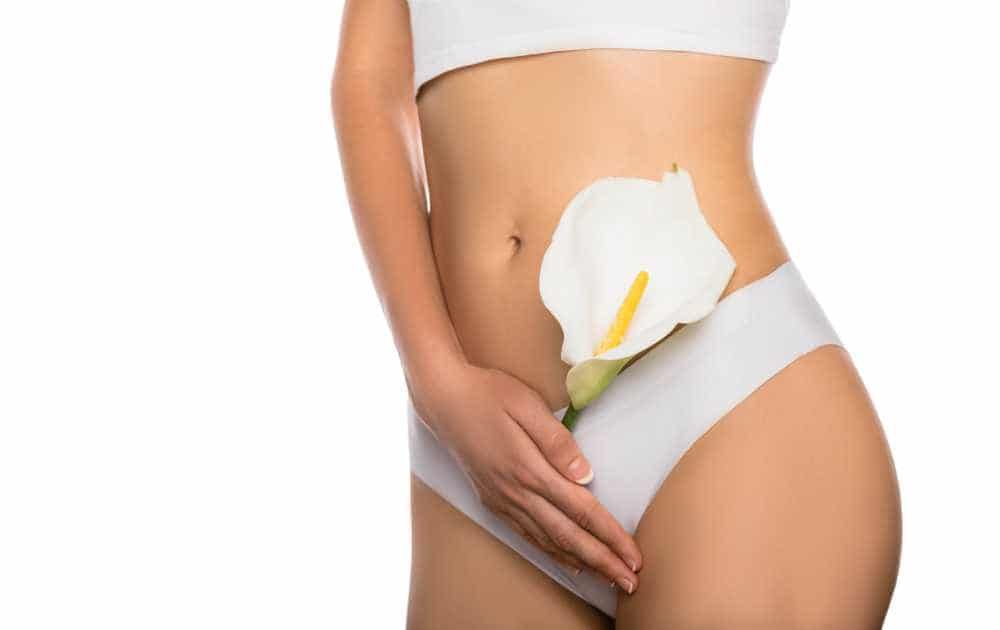 Person in white underwear holding a white calla lily over the hip against a plain background