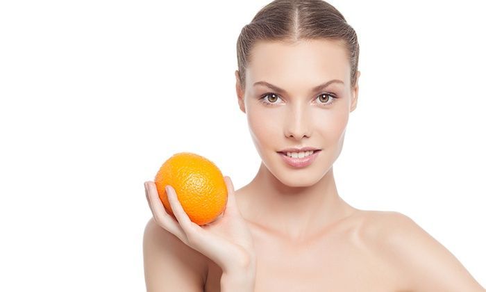 Woman holding an orange close to her face against a white background