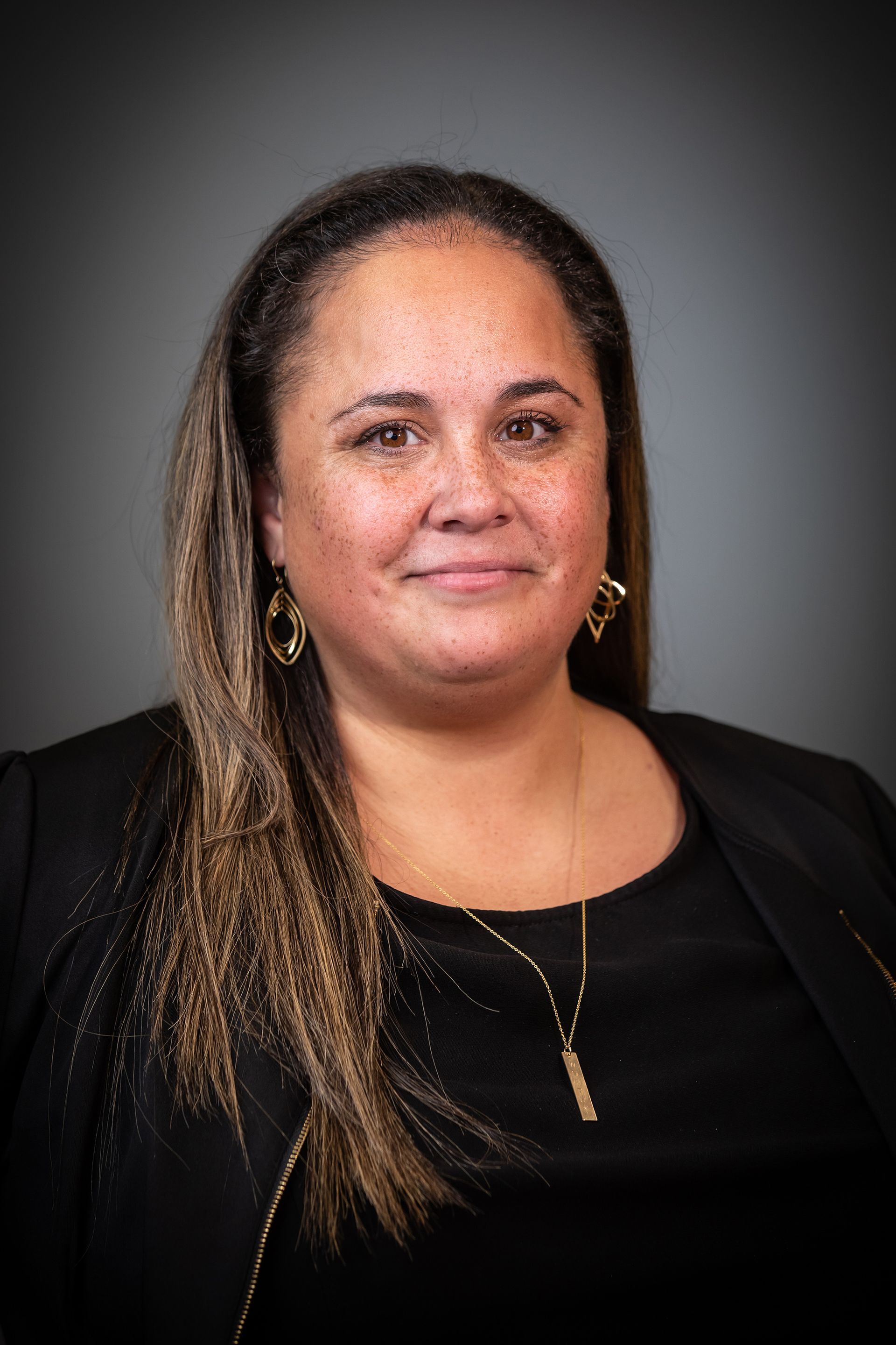 Portrait of a woman in a black top with gold earrings against a gray background