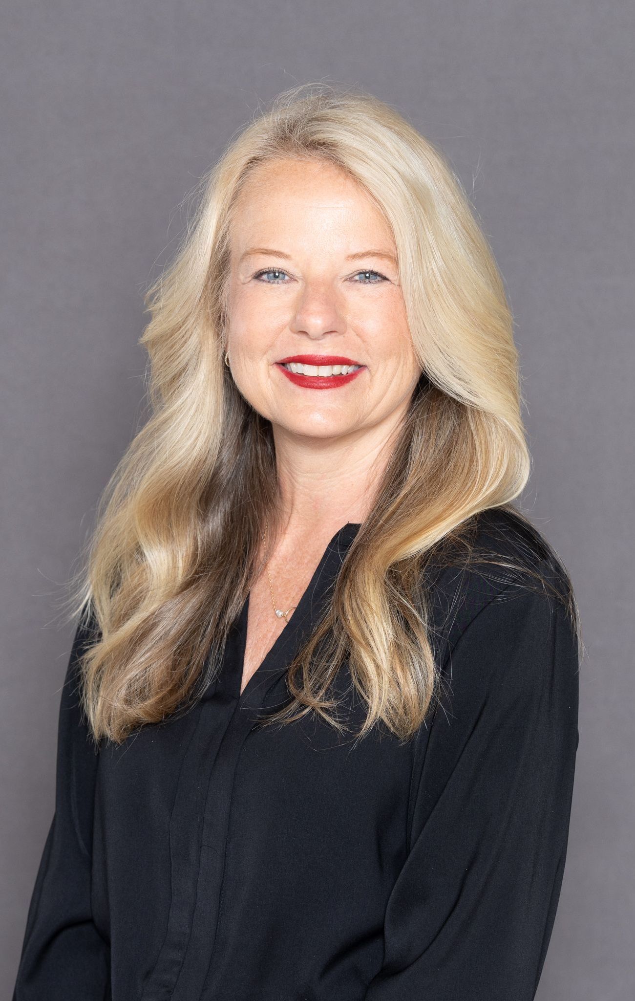 Smiling woman with long blonde hair in a black top against a gray background