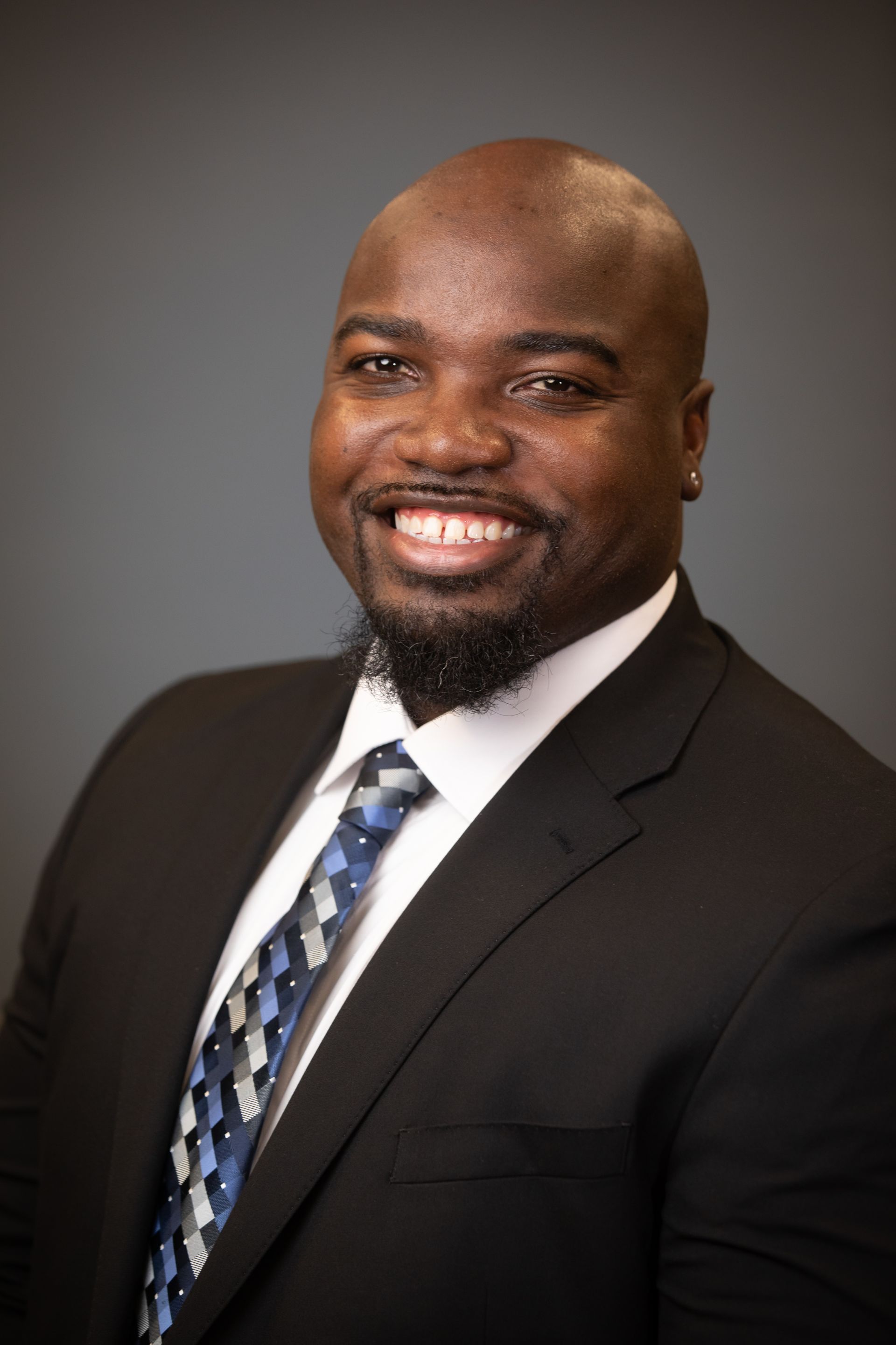 Smiling man in a black suit and blue tie against a gray background