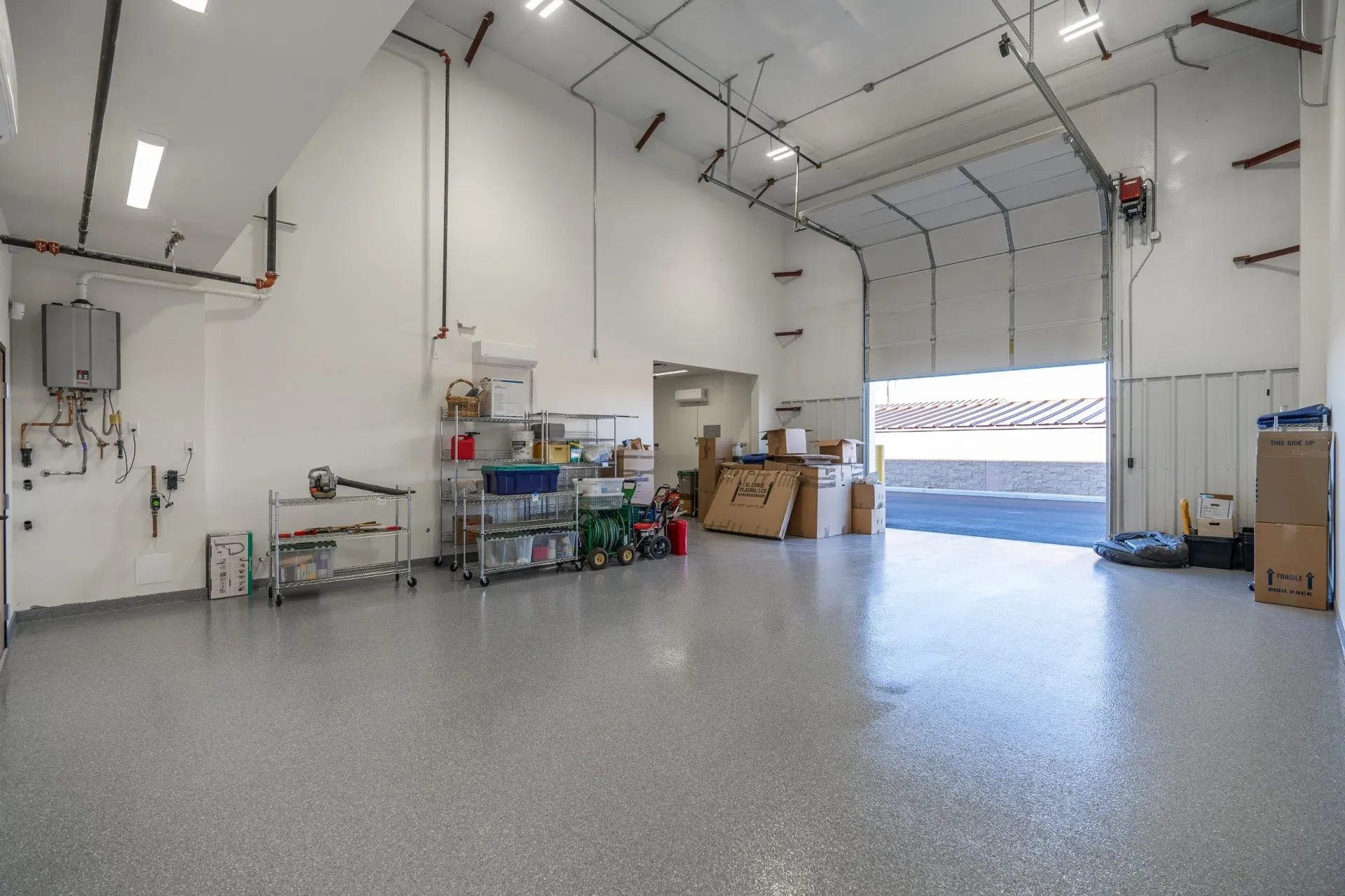 Spacious, empty warehouse with a glossy gray floor and open bay door; various items are stored.