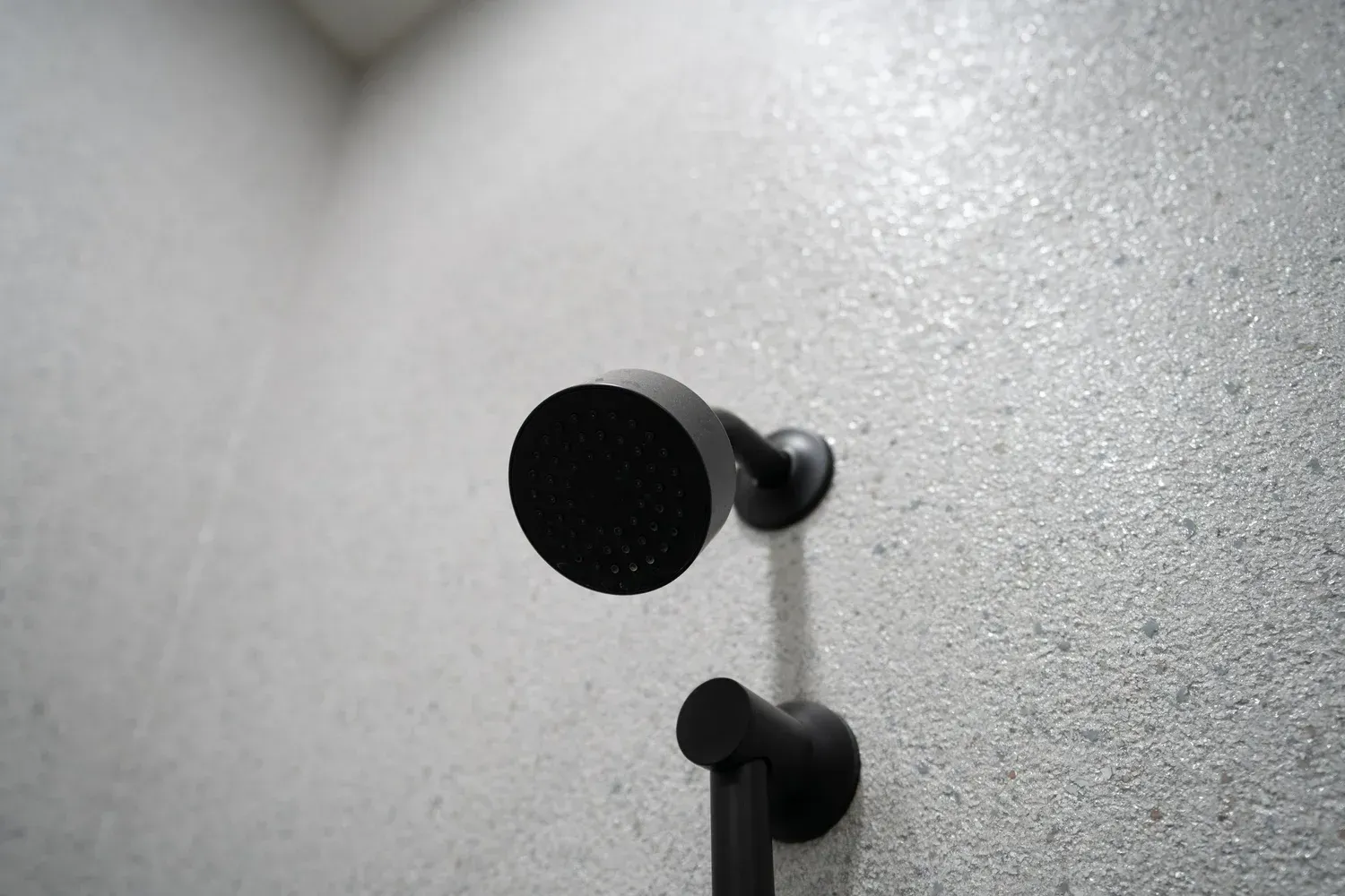 Black shower head on textured, speckled gray wall.