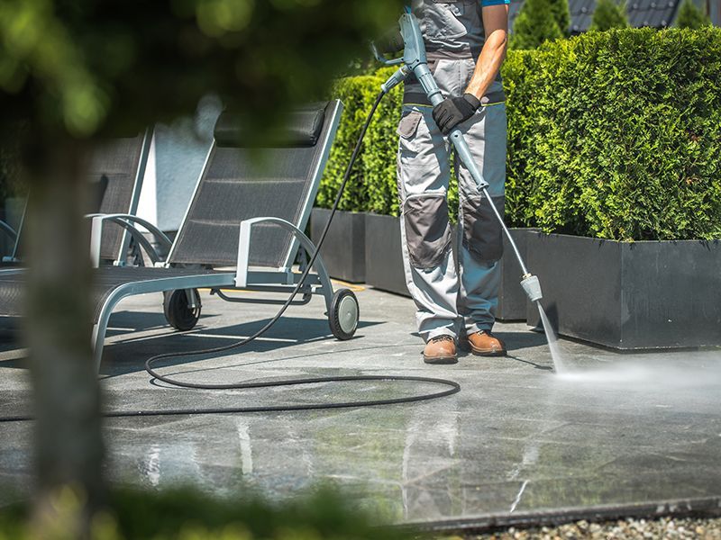 Un homme utilise un nettoyeur haute pression pour nettoyer une terrasse.