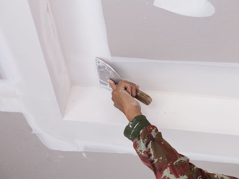 Une personne enduit un plafond avec une spatule.
