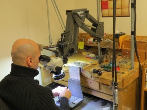 Person examining a microscope in a workshop beside a large metal machine arm