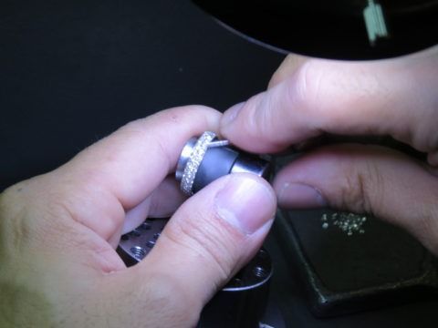 Hands adjusting a silver ring on a black object against a dark background