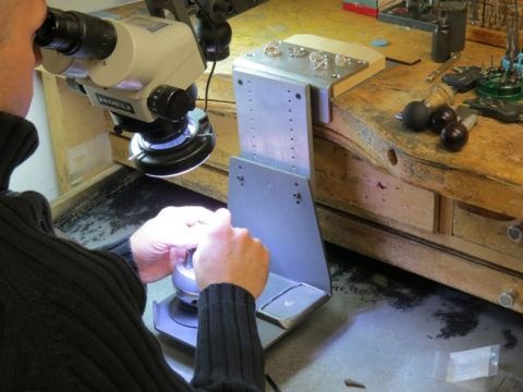 Person using a microscope to inspect a metal part on a workbench in a workshop.