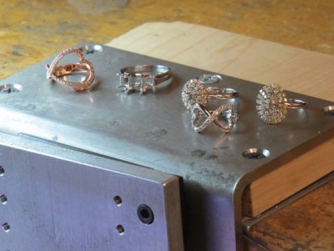 Five silver and rose gold rings displayed on a metal box against a wooden surface