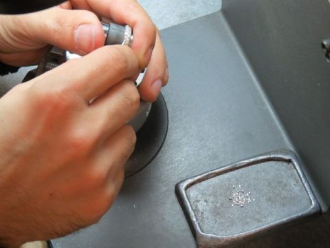 Hands holding a small metal part over a gray countertop with a square drain or cover nearby