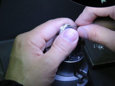 Hands opening a silver ring box with a small item inside on a dark surface