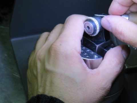 Hands adjusting a silver mechanical device with a small knob in a dim setting