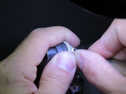 Hands adjusting a silver ring on a dark surface