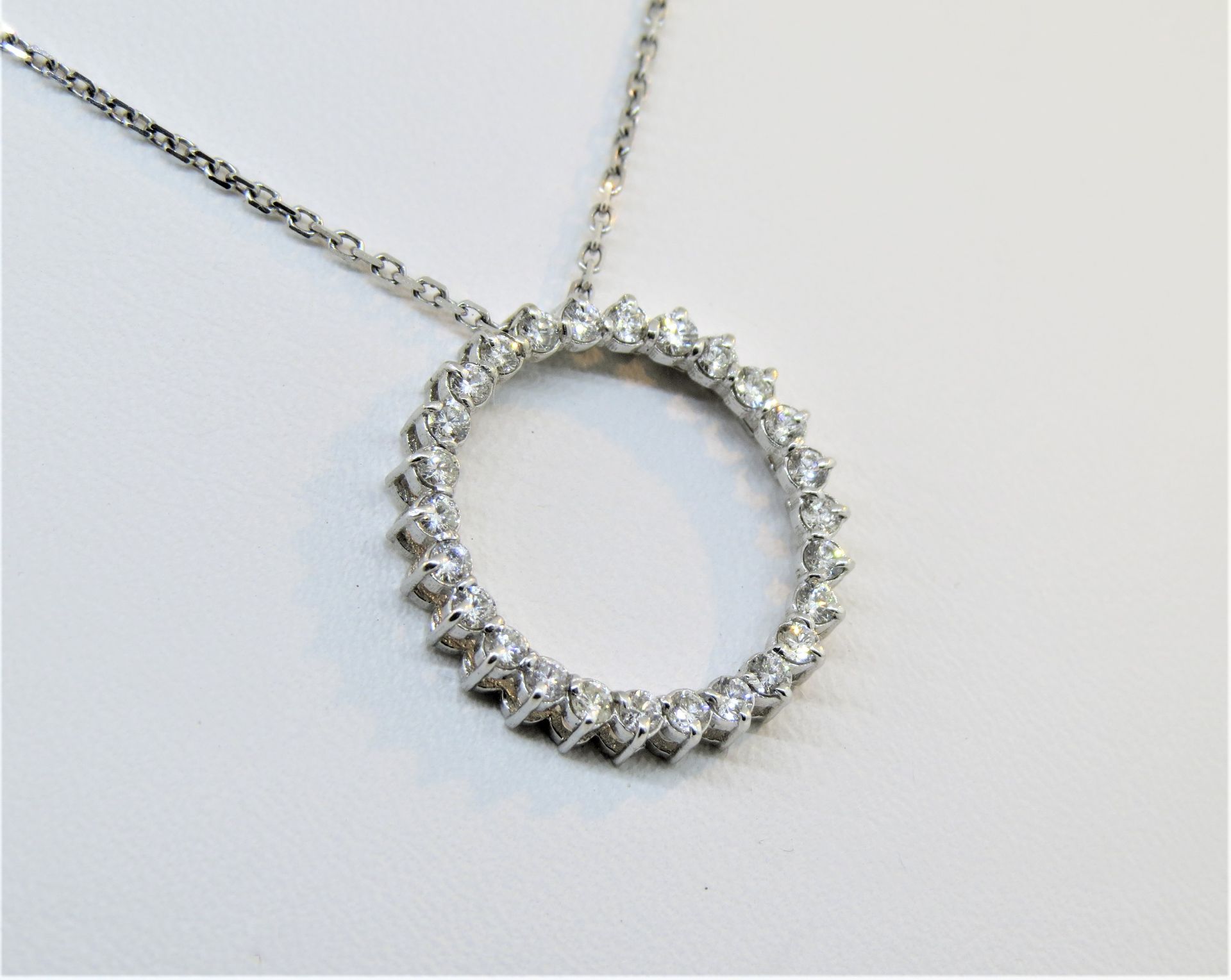 Silver pendant necklace with a circular, gemstone-studded charm on a white background