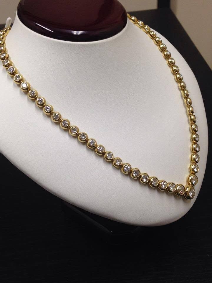Gold beaded necklace displayed on a white bust stand with a dark wooden neck base
