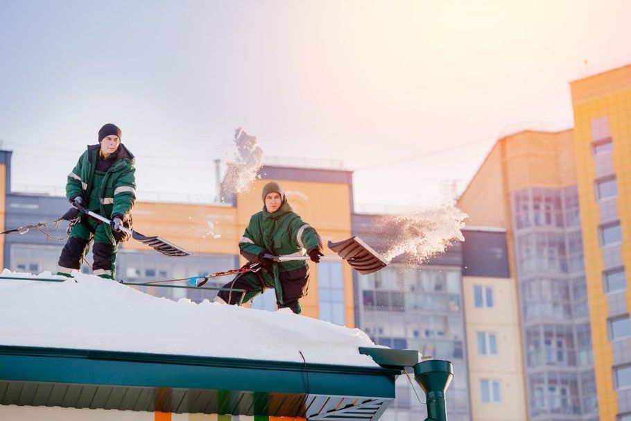 Two skiers in green jackets standing on a snowy rooftop at sunset