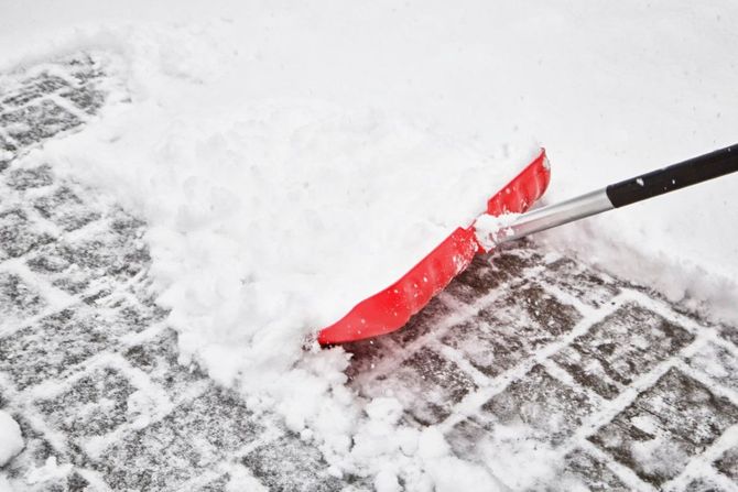 Red snow shovel clearing snow from a tiled walkway