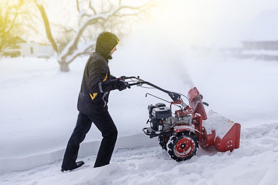 Person clearing snow with a red snowblower in a snowy yard during heavy snowfall